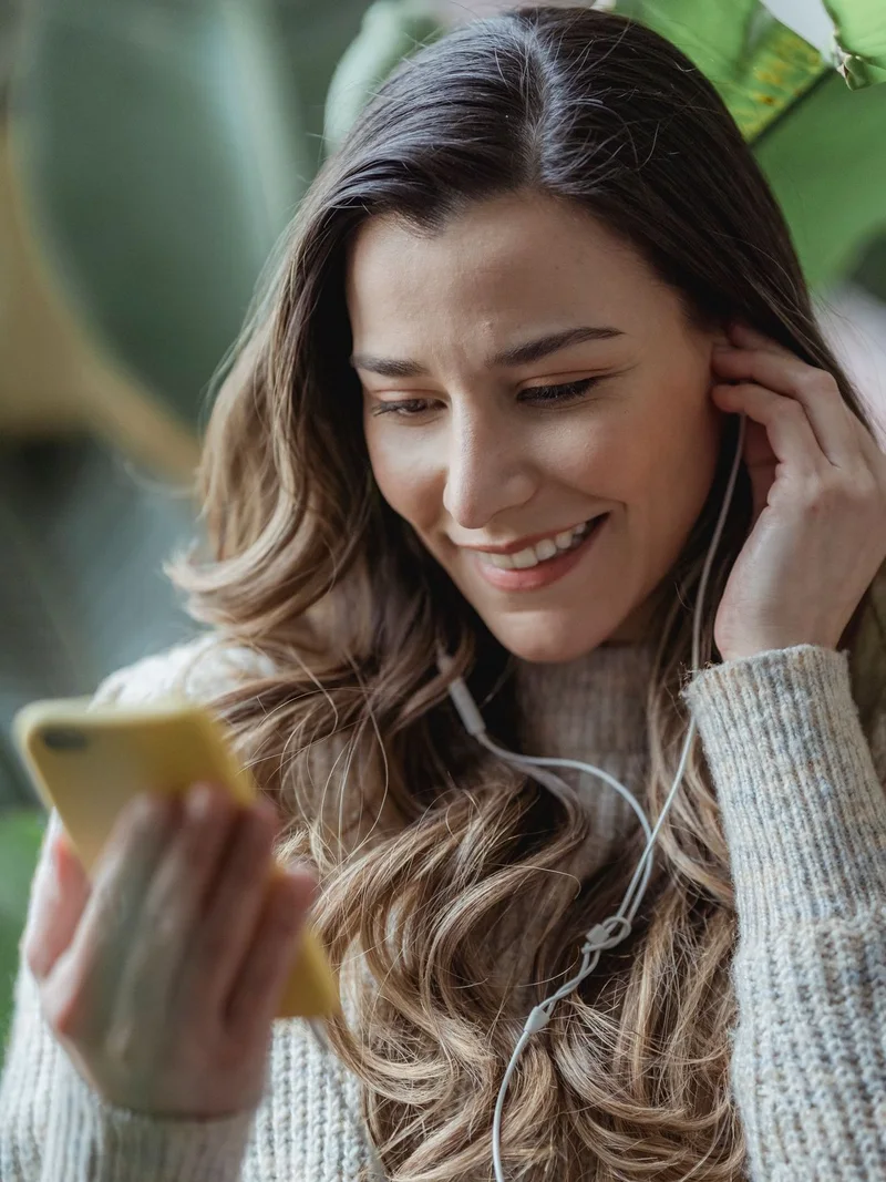 A woman smiling at her phone, wearing earphones