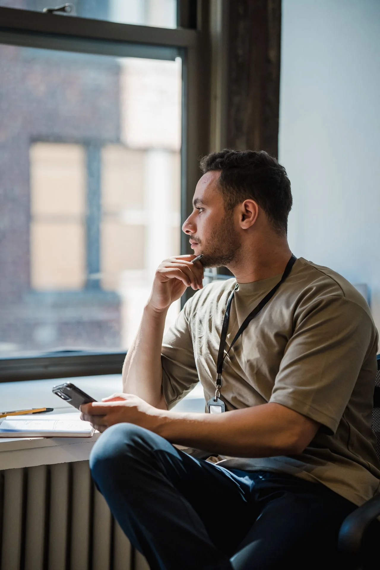 A man at his desk looking out the window, holding his phone